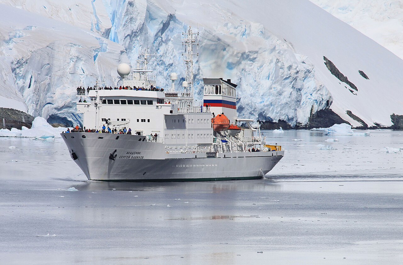 A polar expedition cruise ship gliding through the Lemaire Channel, framed by glaciers and mountains